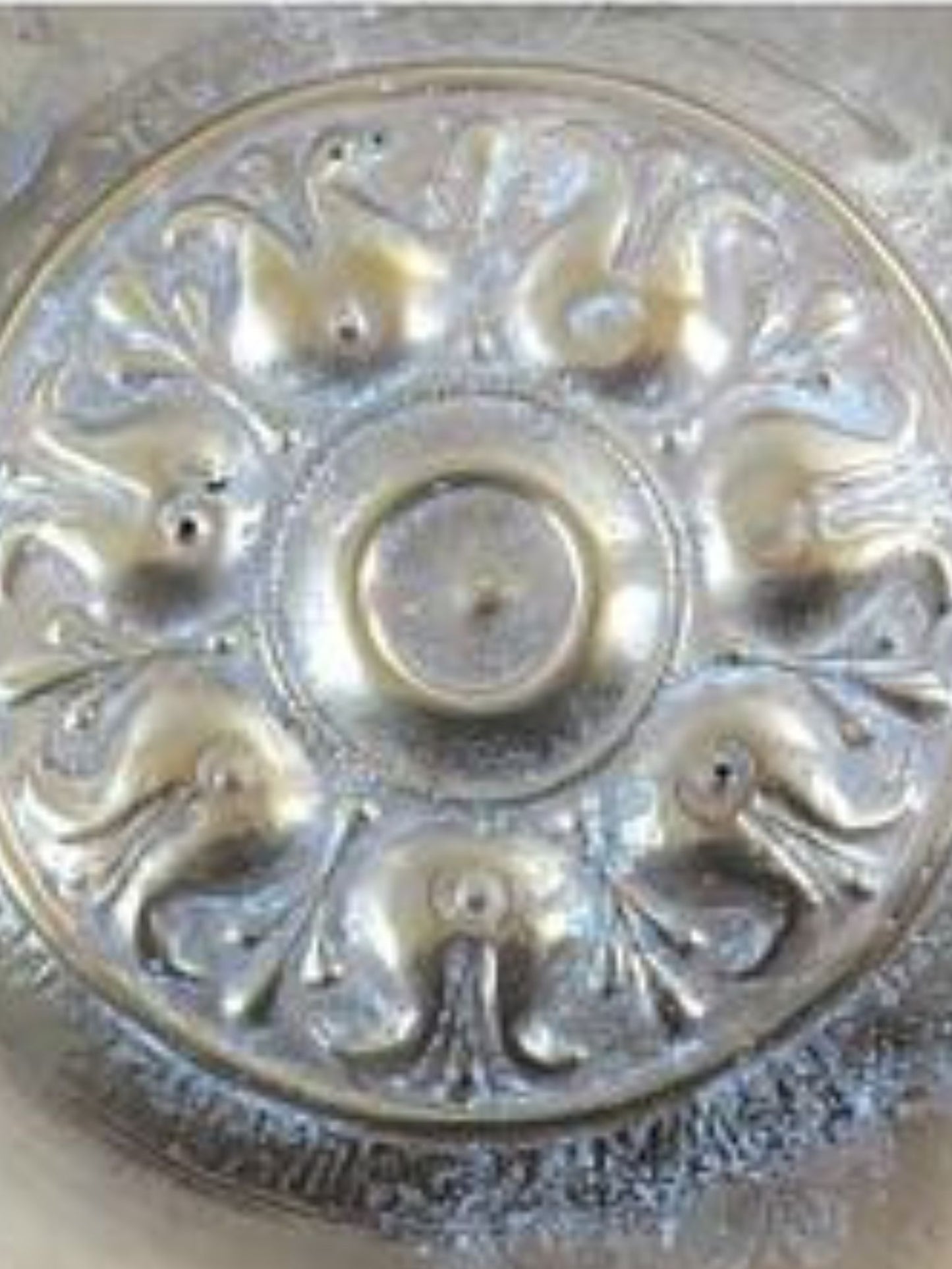Decorative metal object with intricate designs on a beige background