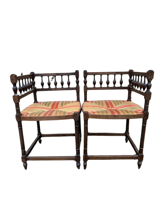 A pair of French rush-seat corner chairs with open backs and decorative carvings, featuring striped multicolor fabric on the seats.