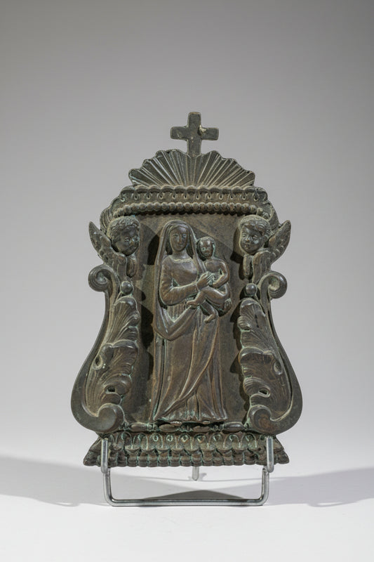 A silver-plated bronze kiss of peace sculpture with the effigy of the Virgin and Child, surrounded by cherubs' heads.