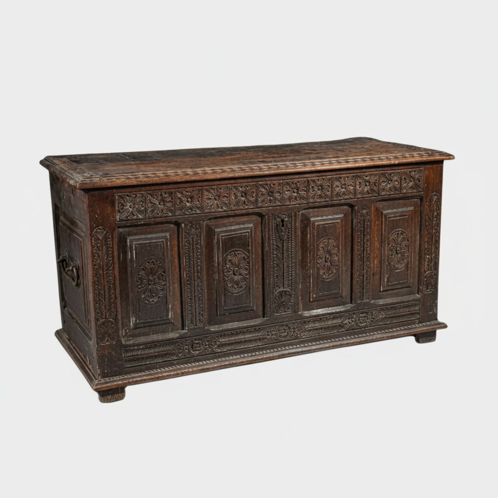 An old walnut chest with intricate carvings, featuring four rosettes on the front and a feathered design on the uprights.