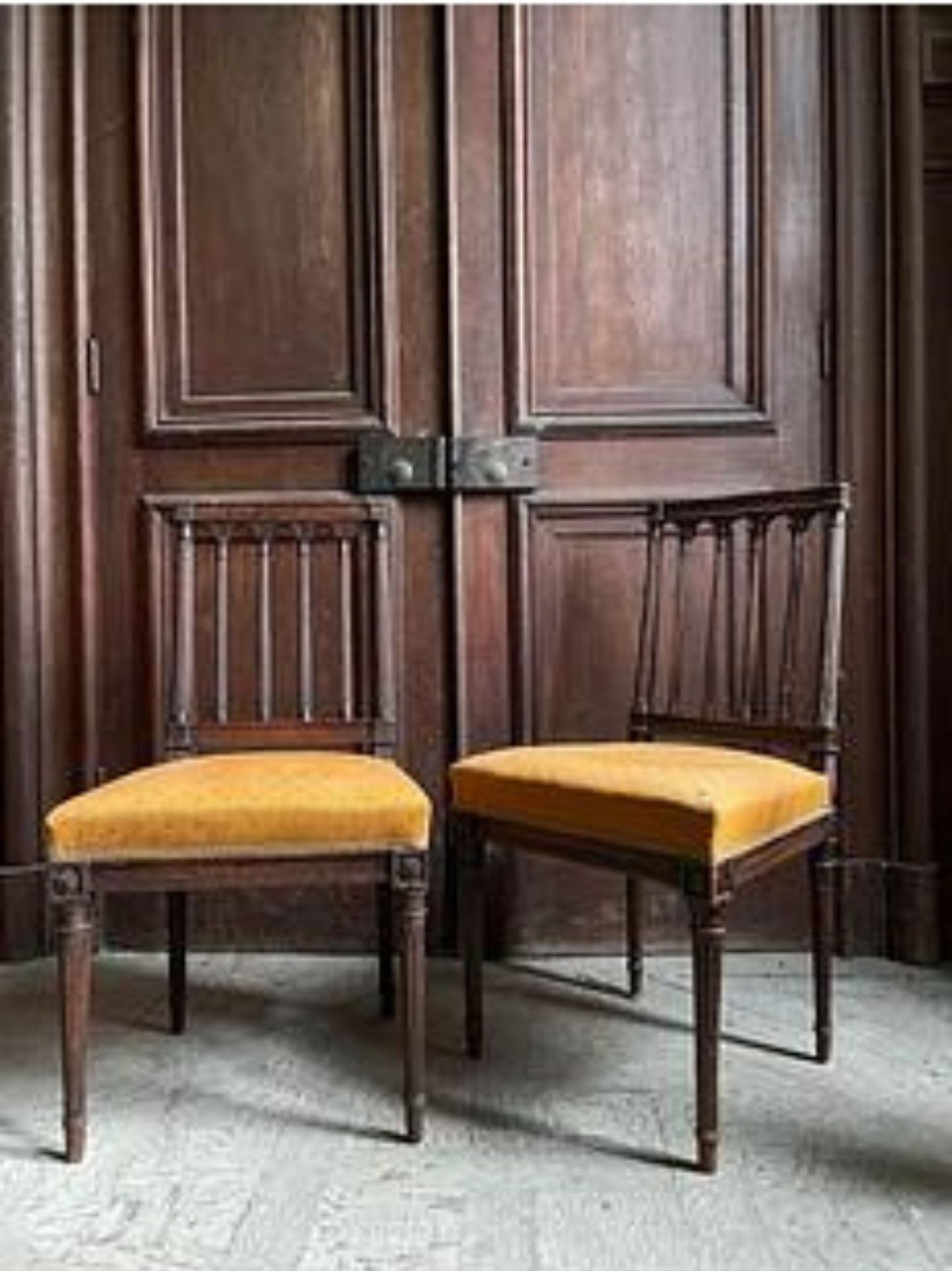 Two wooden chairs with yellow cushions in front of a large wooden door.